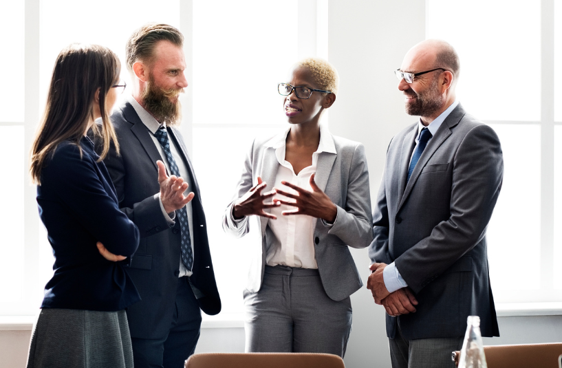 A group of business professionals engaged in discussion during a meeting around a conference table.